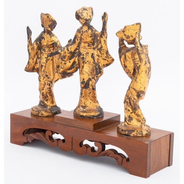 Three James Mont Style Gilt Metal Figural Sculptures, depicting dancing geisha figures, with tiered wood stand. Overall:...