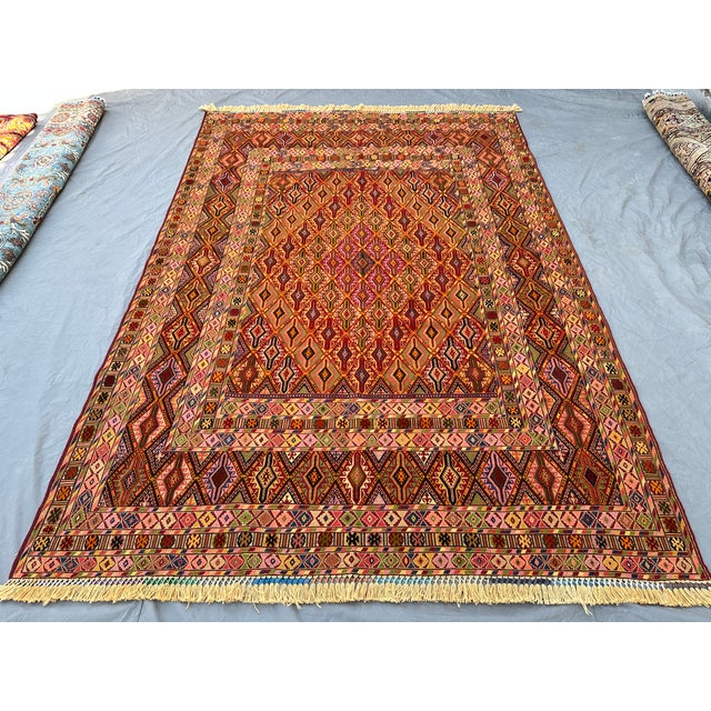 This richly colored Mushwani kilim features a dense allover diamond lattice in deep maroon, olive, gold, and rose,...