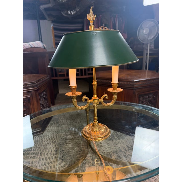 Elegant vintage French Empire–style bouillotte table lamp featuring an ornate brass-tone metal base with two gracefully...