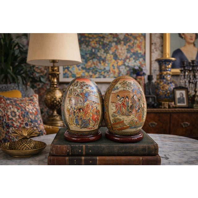 This striking pair of vintage hand-painted porcelain decorative eggs features richly detailed courtly and floral scenes...