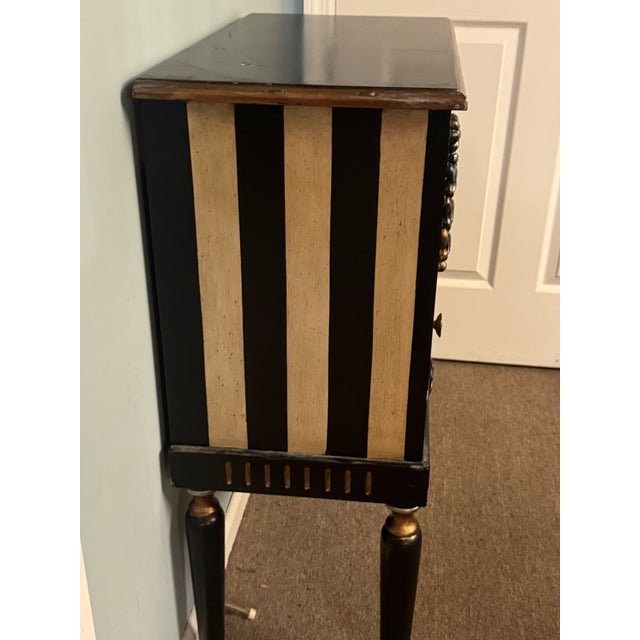 Striking Hollywood Regency–style accent cabinet featuring a dramatic black and gilt striped finish with a painted...