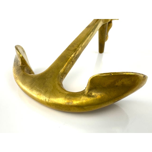 A sculptural mid-century brass candlestick formed as a stylized nautical anchor, balancing functional design with bold...