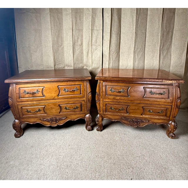 A charming pair of mid-20th century French provincial-style nightstands, each crafted in solid oak with shaped bombe...