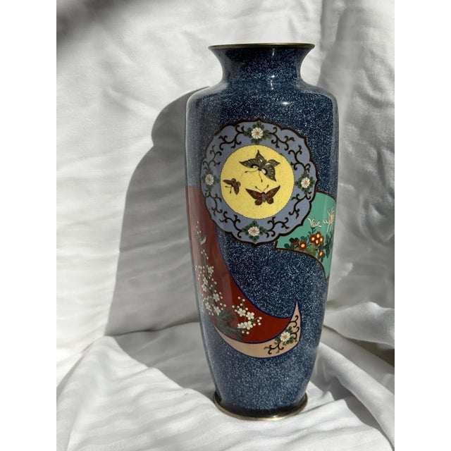 Elegant Japanese cloisonné enamel vase measuring 9½ inches tall, featuring a deep speckled blue ground with a flowing...