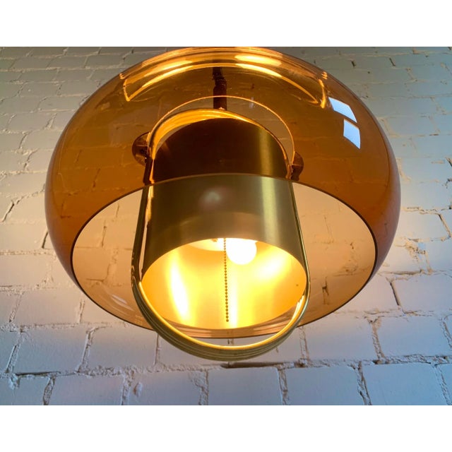 The lamp features a smoked brown acrylic shade combined with gold tone metal details, reflecting the futuristic and...