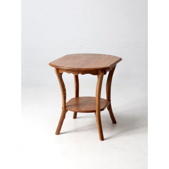 This vintage oak side table features gracefully curved legs and a carved wheat sheaf apron, a classic motif associated...