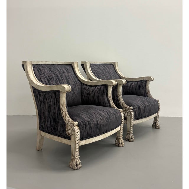 An elegant pair of Neoclassical-inspired bergère lounge chairs featuring a hand-distressed painted frame with carved...