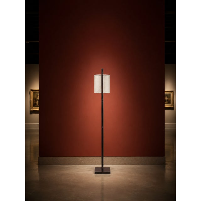 A modern minimalist floor lamp with a clean rectangular frame, square base, and cream fabric drum shade. The frame...