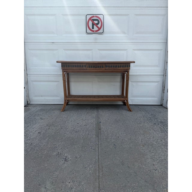 We have an absolutely gorgeous vintage boho rattan console table for sale. It features woven wicker detailing, a center...