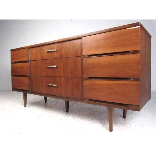 This Mid-Century Modern walnut dresser features nine spacious drawers for bedroom storage, tapered legs and unique drawer...