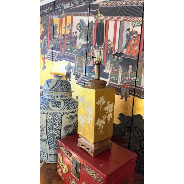 A jewel-like vintage Chinoiserie table lamp combining a luminous gold-leaf ceramic body, hand-painted ivory grapevines and...