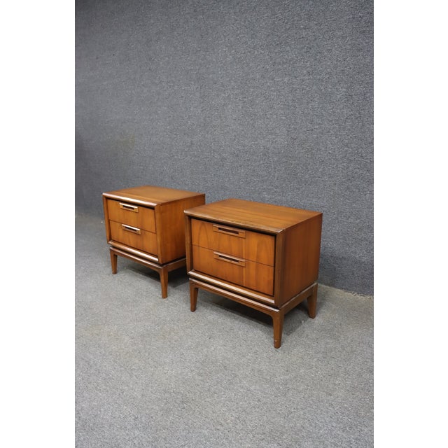 Pair of Mid-Century Modern walnut nightstands attributed to United Furniture Corporation. Each nightstand features two...