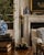 A tall neoclassical candlestick combining warm brass ornament with a slender, fluted black stem. The architectural base is...