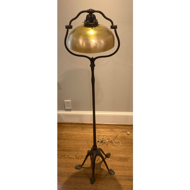 Antique forged iron floor lamp with gold colored glass shade and pull chain switch.