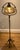Antique forged iron floor lamp with gold colored glass shade and pull chain switch.