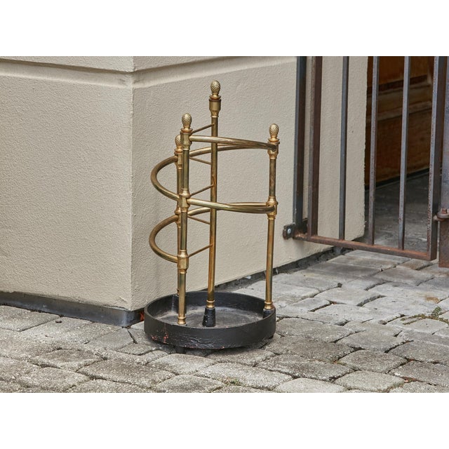 An English Late Victorian era brass umbrella stand from circa 1900 with pinecone motifs and iron base. Embrace the...