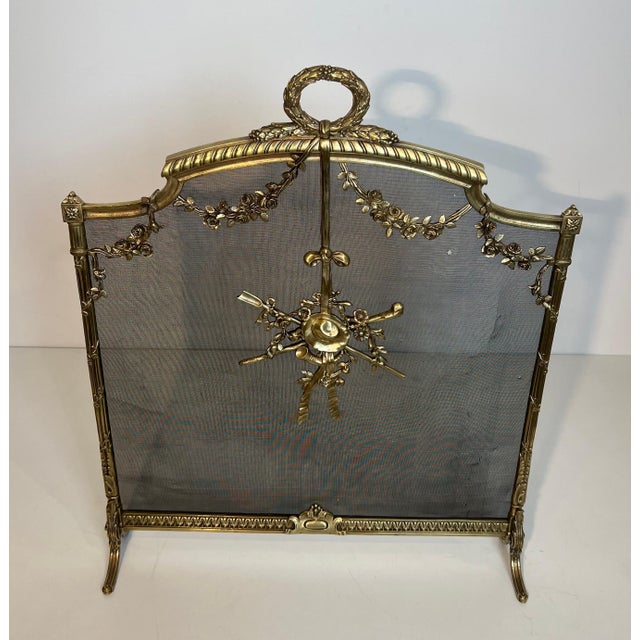 This beautiful fireplace screen is made of brass with netting and is decorated with garlands, a laurel wreath, a hat, and...