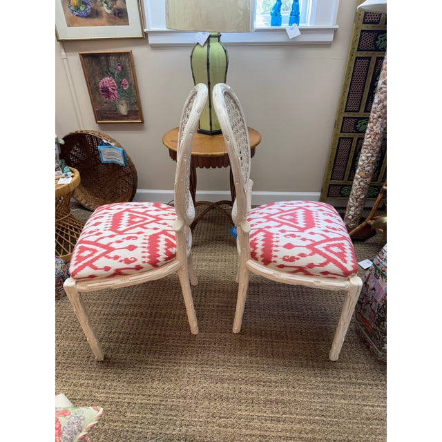 This is a lovely pair of white painted faux bois chairs with linen coral ikat upholstered seats. The cane backs are...