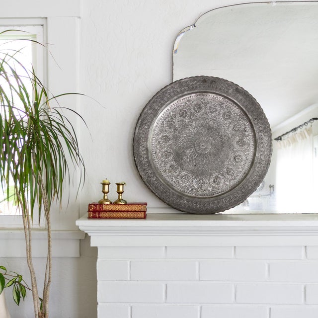 A silver-tone hand-engraved round Ghalamzani Persian tray, featuring intricate repeating patterns of paisleys, foliage,...