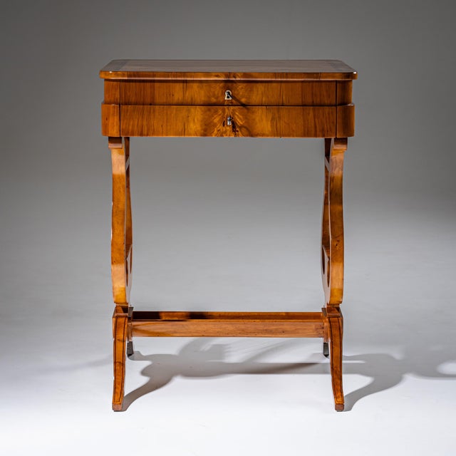 Elegant Biedermeier sewing table veneered in cherrywood. The table rests on a base with lyre-shaped legs decorated with...