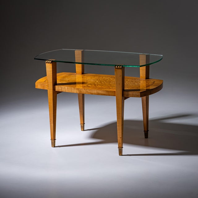 Coffee table with glass top on square tapering legs with brass sabots and intermediate shelf. The glass top is rounded on...