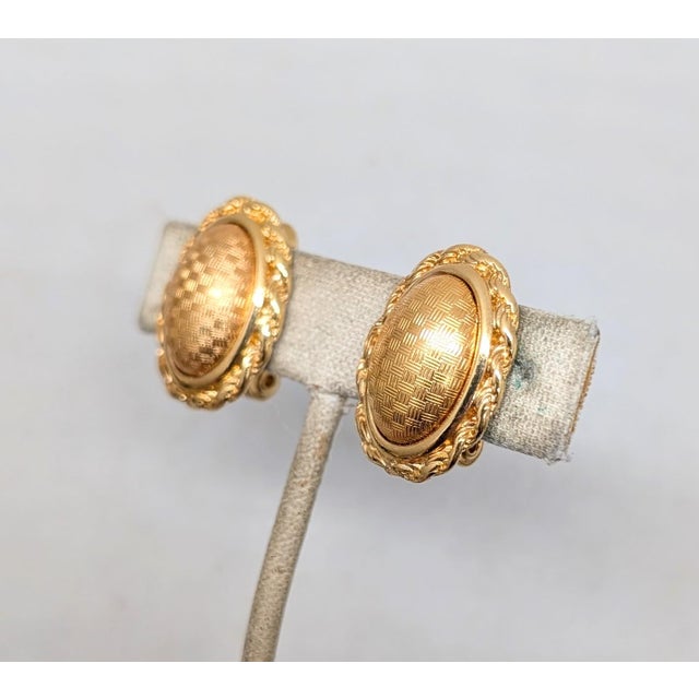 1980s goldtone oval domed with checkerboard pattern with a wrapped edge design clip earrings. Marked "Monet ©" on the...