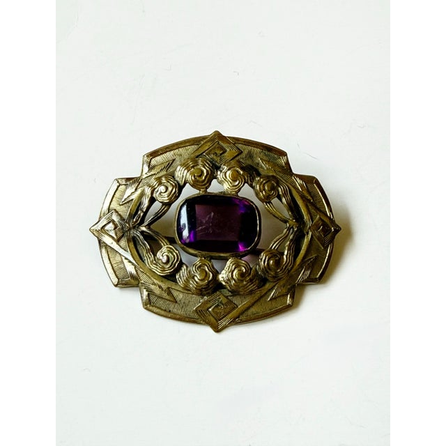 Lovely art nouveau brass sash pin with purple glass or crystal cabochon set center stone. Abstract design. Measures...