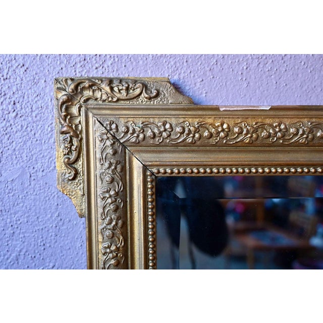 Here's a beveled antique mirror with undeniable flair! The stuccoed wooden frame, adorned with a floral frieze and a...