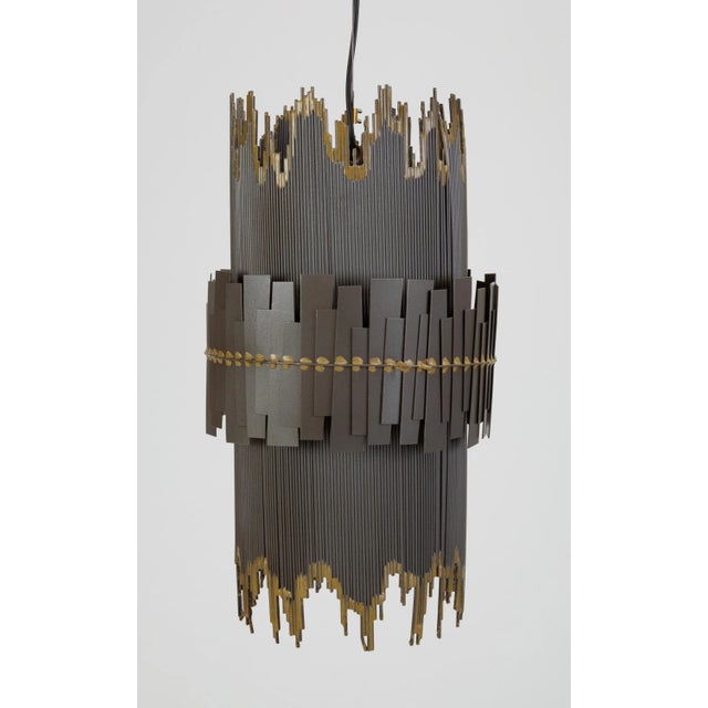 A brutalist metal pendant lamp with a cylindrical shape and irregular edges by Curtis Jeré. The main shape of the Tom...
