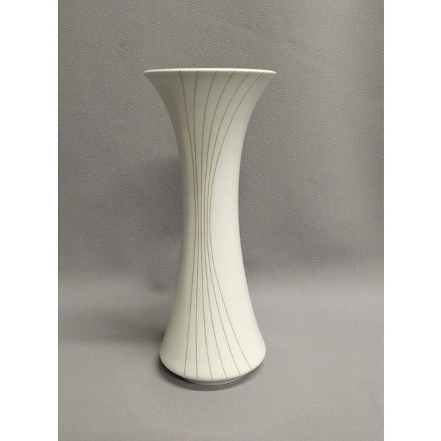 A white German porcelain vase with gold trim and curved lines.. Manufactured by Hutscheneruther, the tall vase has an...