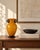 A striking hand-blown art-glass vase featuring a warm ochre-yellow exterior over an opaque white interior. Its full...