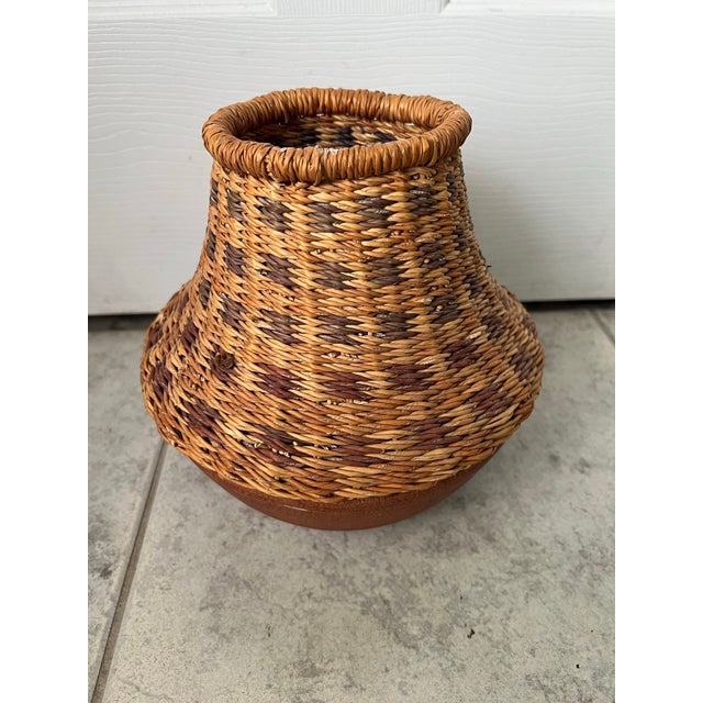 This handmade clay and wicker pot from Ghana features a bulbous terracotta base wrapped with tightly woven natural fibers...