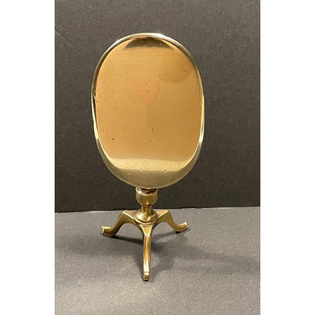 Antique early 19th century brass candle reflector. Oval table form with tripod base, inlaid with a copper heart. This has...