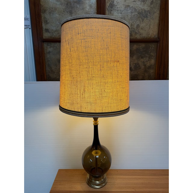 Design Plus Gallery presents a Mid 20th Century Table Lamp. The lamp pairs an olive smoke glass bottle-form body with...