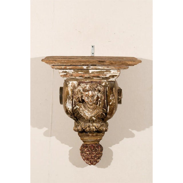 An 18th century architectural gilded and painted wood bracket with carved angel and pine cone finial.