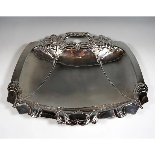 Wide silver bowl in a trapezoidal shape standing on four appliquéd feet, one-sided handle in the extension of two relief...