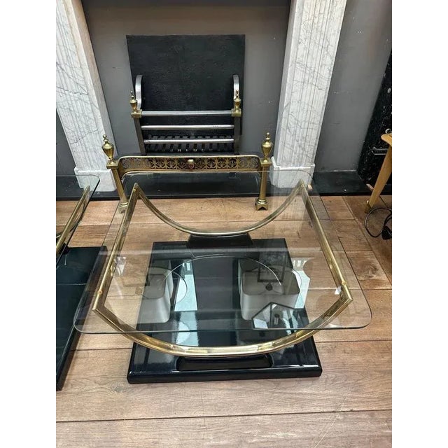 A pair of large end or side tables with square black lacquered bases and semi circular brass supports, the glass tops with...