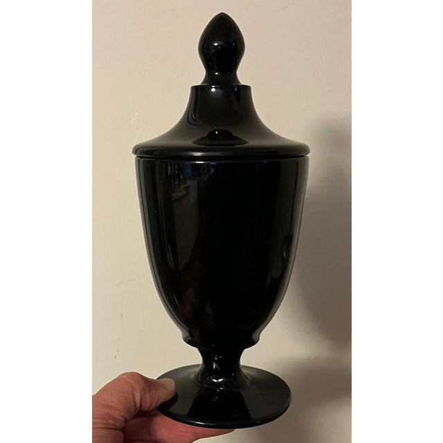 Black amethyst glass urn with cover. Vase shaped jar rising on a round foot. Measures 8 3/4" tall x 3 7/8" diameter. Good...