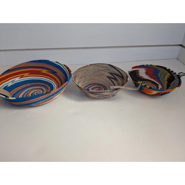Trio of Colorful African Handwoven Baskets Design: A vibrant and eclectic trio of handwoven African baskets, each...
