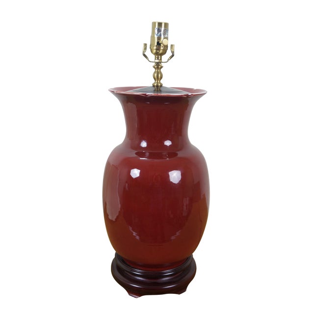Late 20th century Chinoiserie vase shaped oxblood red porcelain table lamp with wooden base. Includes harp, pink glass orb...