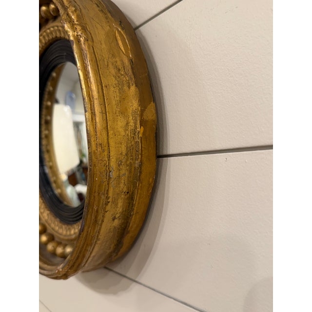 This antique English convex mirror is styled in the Regency fashion with a signature gilt gold frame and ebonized black...
