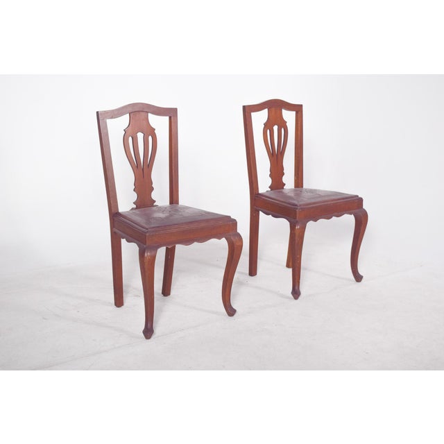 Pair of chairs with embossed leather seats. with a design inspired by the Queen Anne style, they feature elegant, curved...