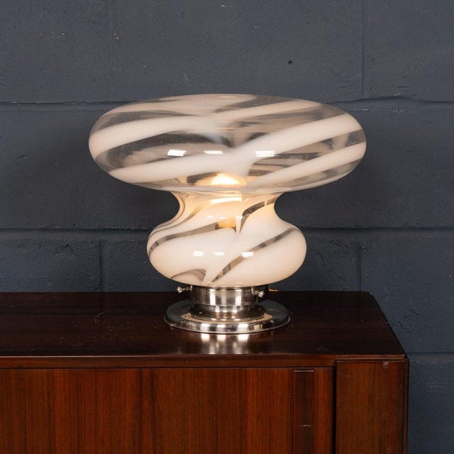 A striking italian table lamp dating to the 1970s, featuring a sculptural murano glass shade with bold white swirling...