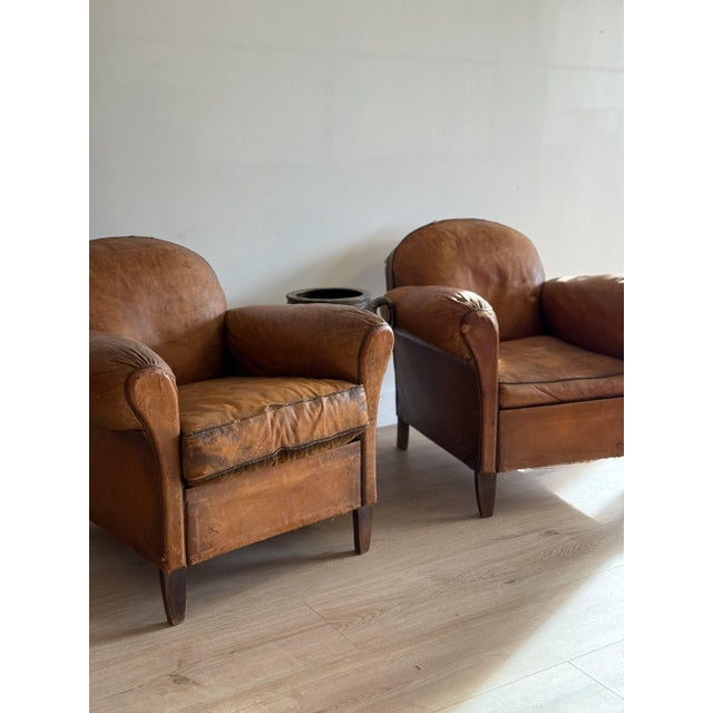 A pair of French club chairs from the 1920s with rounded backs, rolled arms, and deep seats that invite you to sink in....