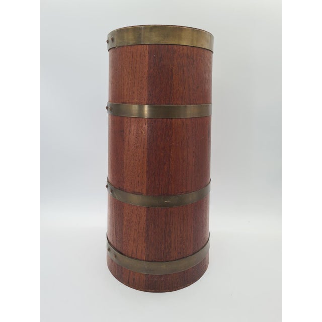An elegant umbrella stand made of solid wood in a warm mahogany tone, accented with decorative brass bands. The form draws...