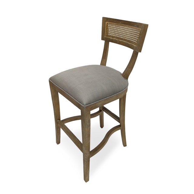 The Carvell Cane Back Bar Stool from Zentique in grey linen pairs the klismos-inspired silhouette with a woven cane back...