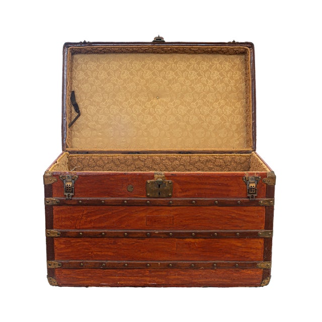 Steamer trunk, featuring a sturdy wooden frame reinforced with robust brass fittings, corner guards, and rivets, retaining...