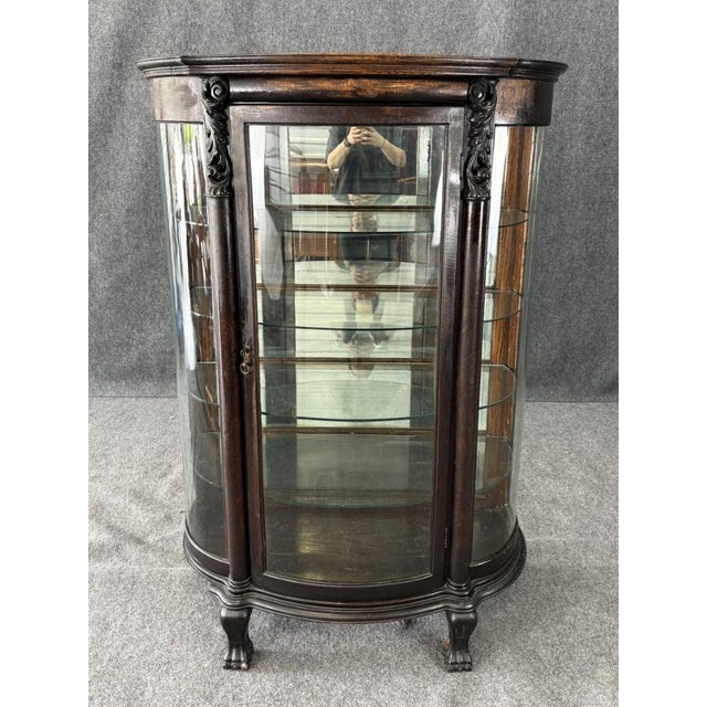 This elegant early 1900s curio cabinet features a graceful bowed front with glass-paneled sides and door, offering a...