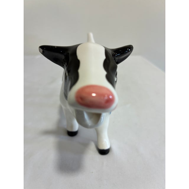 A whimsical vintage ceramic cow creamer in glossy black and white, with a pink nose, a sweet painted face, and a blue bow...