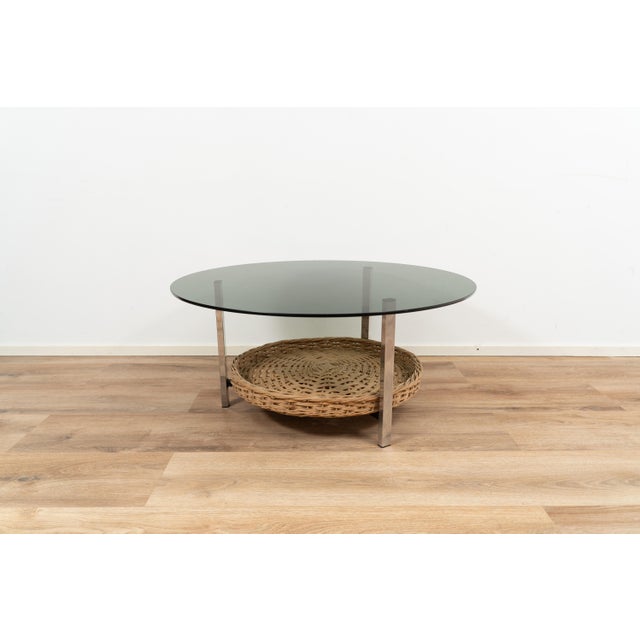Coffee table by Rohé Noordwolde. The piece has a glass top on a chromed metal frame. It comes with a rattan basket in the...